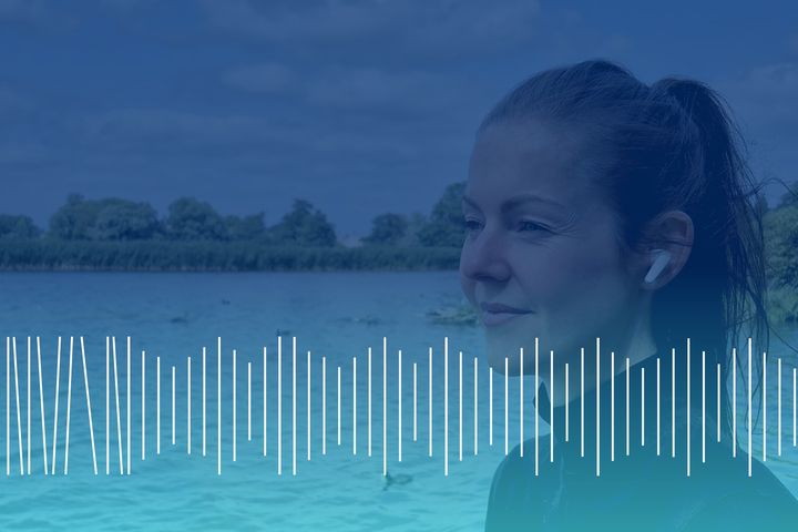 Kvinde med hovedtelefoner står ved en sø med træer i baggrunden. Lydgraf vises nederst.