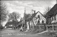 Gadebillede fra Hellested med flere huse, træer og personer langs en vej.