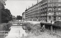 Sort-hvidt foto af en historisk bygade med en kanal, bro og store bygninger langs vejen.
