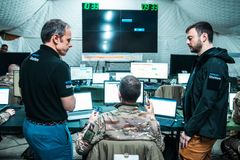 Systematic team and French Army working with laptops in a command center. A large screen displays digital information in the background.