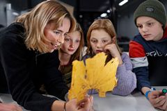 En ung gymnasieelev holder et blad frem og fortæller engageret til en gruppe nysgerrigt lyttende børn