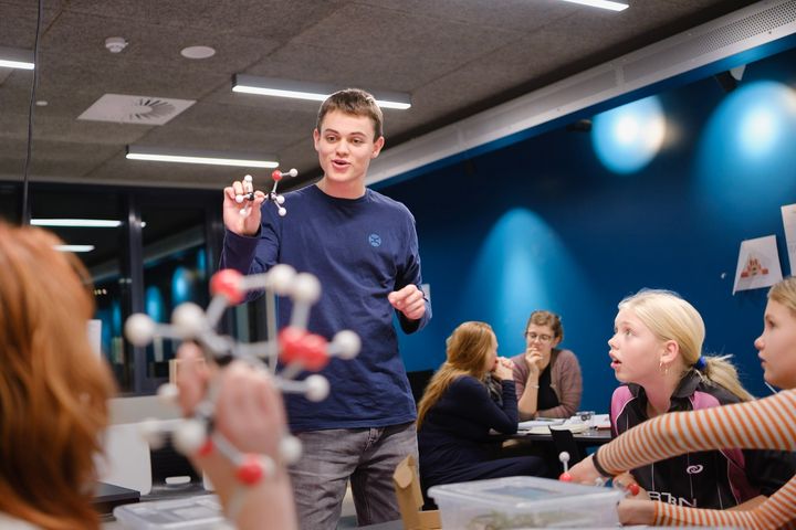 Gymnasieelev forklarer passioneret en gruppe børn om molekylestrukturer