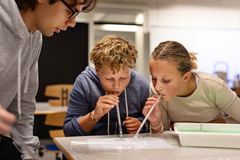 To børn puster til en bakke med sæbevand ved hjælp af sugerør, mens en ung dreng står og kigger på dem.