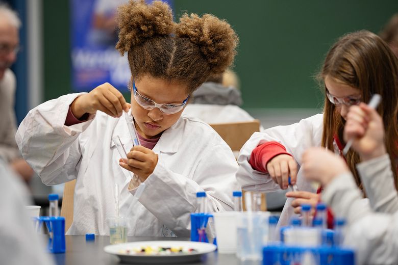 To unge piger i kittel er dybt koncentrerede om et kemiforsøg.