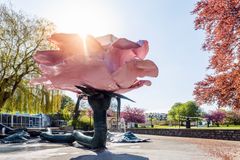 En stor skulptur af en pink blomst i en park med træer og sollys i baggrunden.