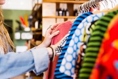 Person ser på forskellige farvestrålende tøjstykker i en butik.