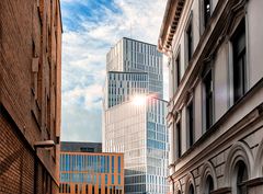 Et højhus ses mellem to ældre bygninger under en skyet himmel.