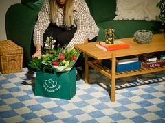 Bilde av en dame som har hentet hjem en forundringspose fra Too Good To Go med roser og orkideer.