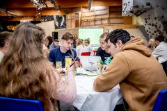 Fem unge sidder om et bord og arbejder om en computer og en masse papir og papkort. Det er et stort rum med en klatrevæg i baggrunden.