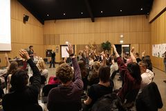 En masse unge sidder i et stort lokale og rækker hænderne i vejret. Foran dem står en person og præsenterer.