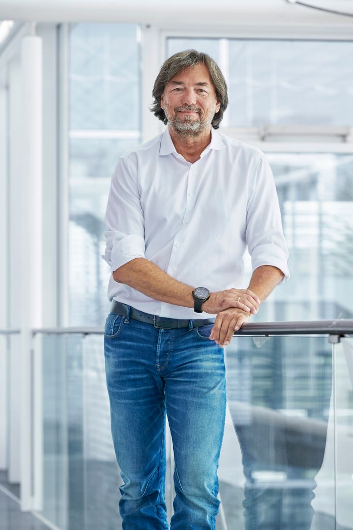 Alt text: A man in a white shirt and jeans stands leaning on a railing in a modern building.