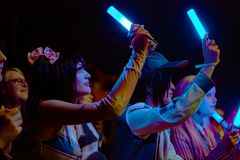 Personer i publikum sidder med lysende, farvede rør i mørke.