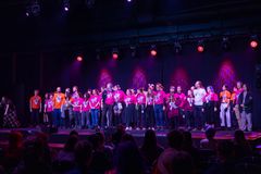 Mennesker i pink og orange t-shirts står på en scene med armene om hinanden.