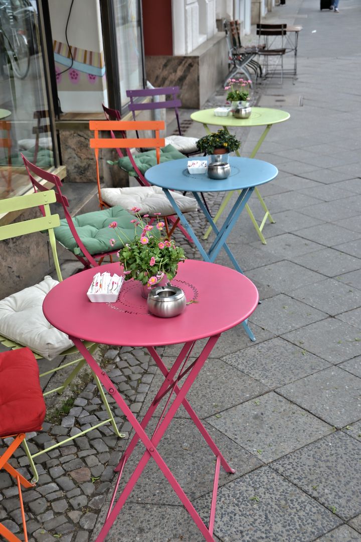 Farverige caféborde på række foran en vinduesfacade.
