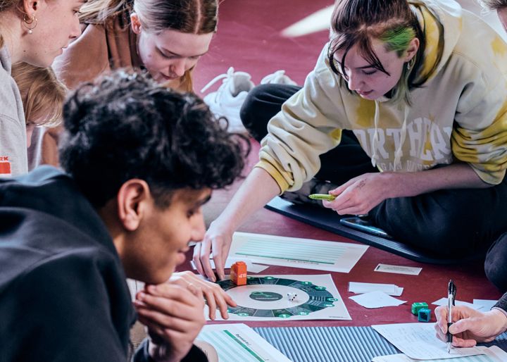 En gruppe unge sidder på gulvet og deltager i en spilworkshop.