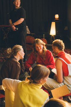 Fire mennesker sidder sammen på gulvet og snakker. Den ene har et brev i hånden. Lyset er varmt. De smiler. Generation Hope viser unge veje til at dele deres håb for fremtiden