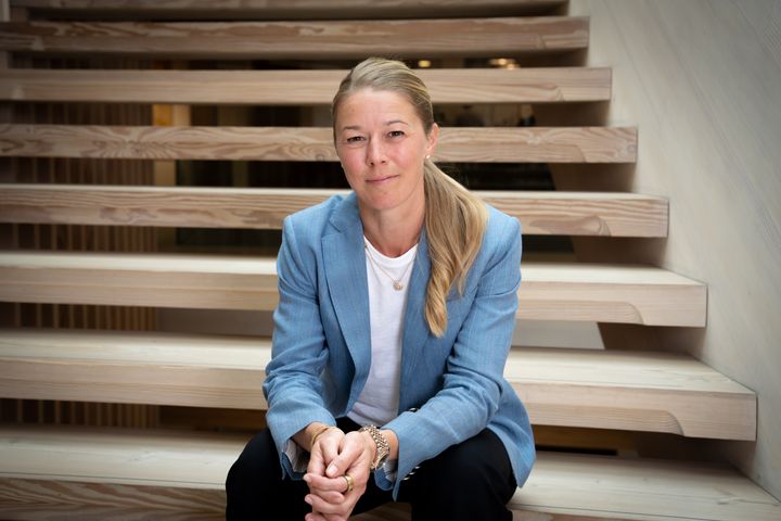 Agnete Kirk Kristiansen i lyseblå blazer sidder på en trappe og kigger mod kameraet.