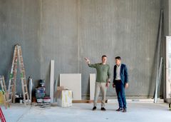 Regionsdirektør René Christensen og afdelingsdirektør Claus Ring Skibsted står i en bygning under renovering med værktøj og materialer omkring dem.