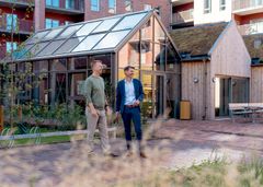 Regionsdirektør René Christensen og afdelingsdirektør Claus Ring Skibsted går i en moderne beboelsesgård med bygninger, der har grønne tage og store vinduespartier.