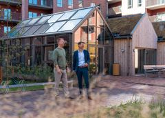 Regionsdirektør René Christensen og afdelingsdirektør Claus Ring Skibsted går i en moderne beboelsesgård med bygninger, der har grønne tage og store vinduespartier.