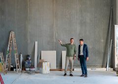 Regionsdirektør René Christensen og afdelingsdirektør Claus Ring Skibsted står i en bygning under renovering med værktøj og materialer omkring dem.