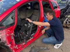 En mand undersøger plastkomponenter i en rød bil på en skrotplads.