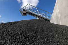 En stor bunke af biokul ved siden af en industrihal og en transportør under en blå himmel.