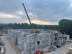 Et byggeplads med en kran, der arbejder på en stor struktur lavet af betonblokke.