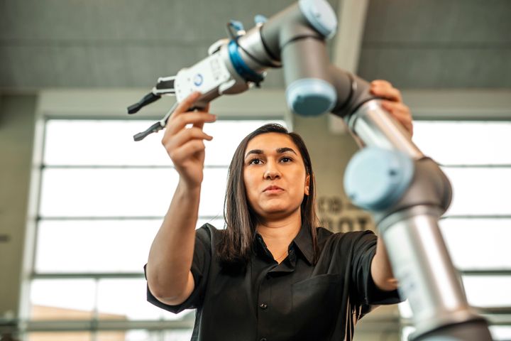 En person arbejder med en industriel robotarm indendørs.