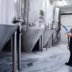 Person rengør store ståltanke med en vandslange i en industriel facilitet.