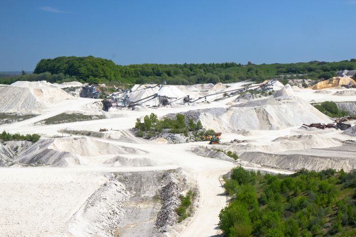 Billede af et stort grusgravsområde med sanddynger og maskiner, omgivet af skov.