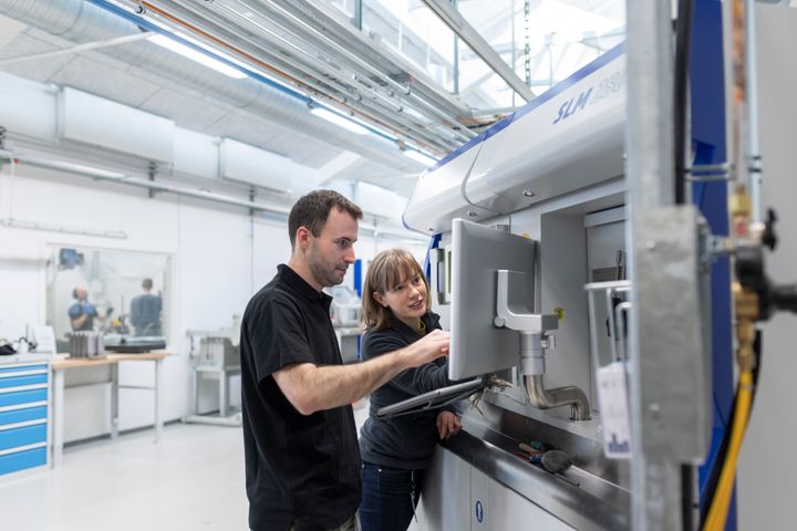 To personer arbejder ved en 3D-printer i et laboratoriemiljø.