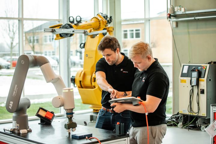 To personer arbejder med robotarme i et værksted.
