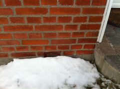 På billedes ses sne ved sokkel, hvor ventilationsrist til udluftning af krybekælder er tildækket af sne. Smeltevandet trænger ind ved tøvejr.