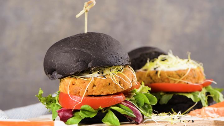 To plantebaserede burgere med sorte boller og friske grøntsager.