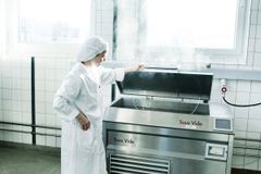 En person iført hvid kittel og hårnet arbejder ved en stor sous vide-maskine i et køkken.