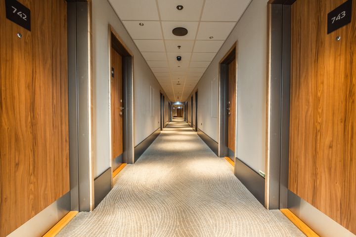 Alt text: En lang hotelkorridor med tæppebelagt gulv og trædøre på hver side.