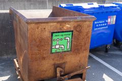 Rustik metalcontainer med skiltet "Jern og metal" ved siden af en blå affaldscontainer.