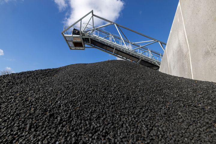 Stor bunke af biokul under en klar blå himmel ved en industrifacilitet.