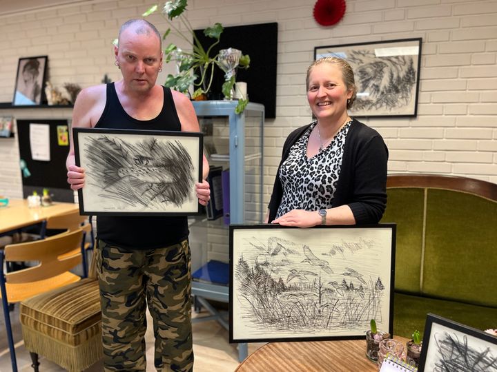 Kim Berndorffs (t.v.) tegninger hænger allerede på væggen på Den Blå Viol. Nu håber både han og værestedsleder Lenette Schultz Nielsen (t.h.), at lokale i Skive har lyst til at købe hans værker. Foto: Blå Kors.
