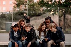 En gruppe unge sidder tæt sammen udenfor og kigger på deres smartphones.