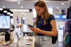 Ung kvinde kigger på en mobiltelefon, mens hun står ved en disk i en butik med produkter.