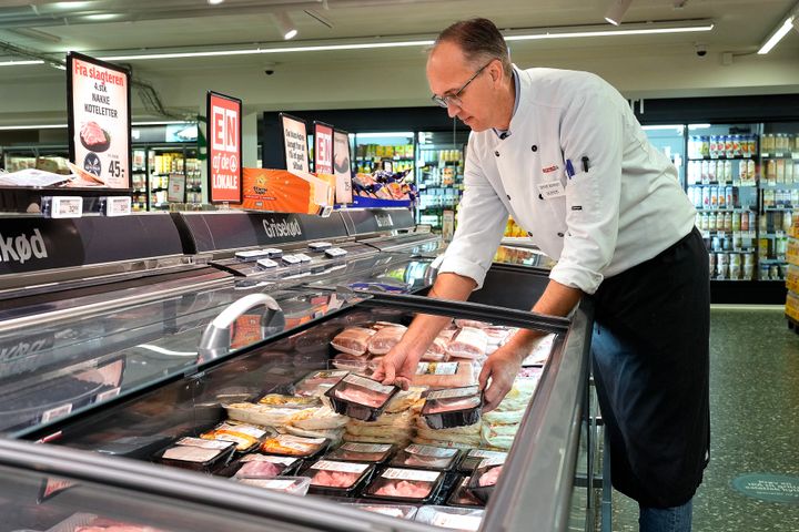 Slagter ordner kød i køledisk i købmandsbutik