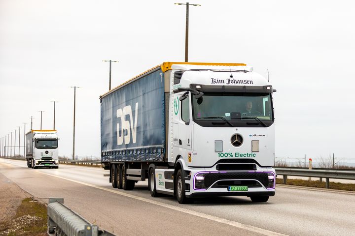 To elektriske lastbiler kører på en vej.