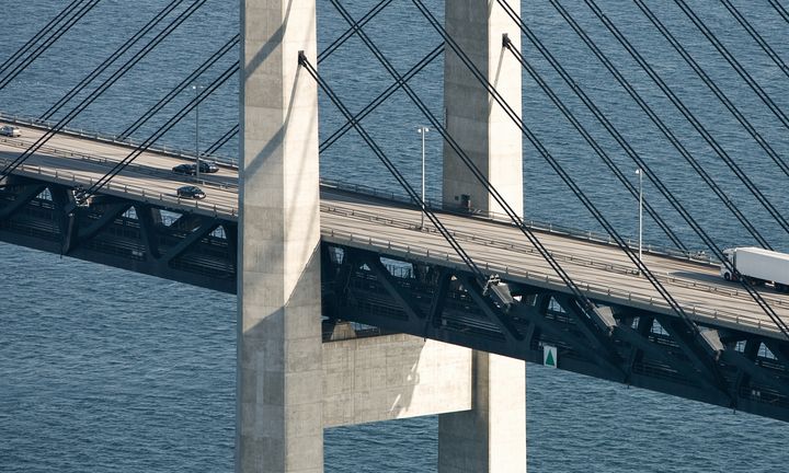 Luftfoto af Øresundsbroen med biler og en lastbil på vejbanen, set oppefra med skråstag og broens pyloner over vandet.