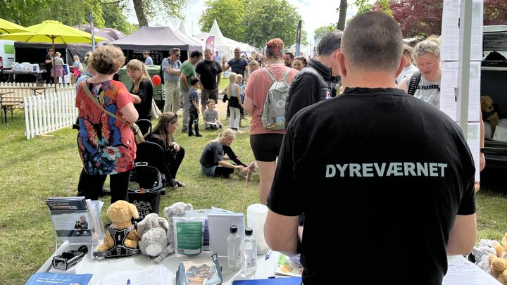 Billede af Dyreværnets stand på Roskilde Dyrskue i 2025. På billedet ses en mand stå på stand, og på ryggen af ham står der Dyreværnet. Foran ham står en masse mennesker på en græsplæne, og der er udsigt til flere stande på dyrskuet.
