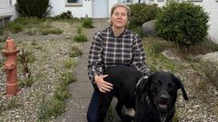 En kvinde i ternet skjorte sidder udendørs med en sort hund.