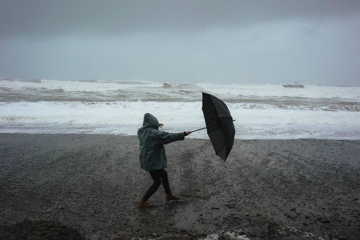 Blæsevejr på en strand, hvor en mand forsøger at holde sin paraply.