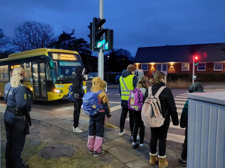 B%F8rn%20og%20voksne%20if%F8rt%20refleksveste%20st%E5r%20ved%20fodg%E6ngerfeltet%20foran%20en%20bus%20i%20%D8stjylland.
