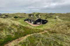 Sommerhus beliggende blandt klitter og græs under en overskyet himmel.